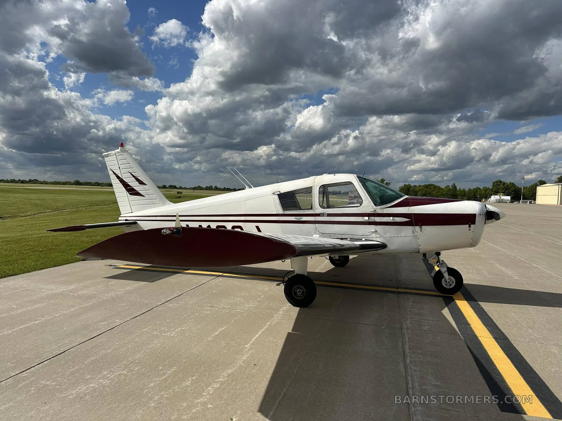 A white and maroon single-engine propeller aircraft, registration N4120J, is parked on an asphalt ramp under a partly cloudy sky, viewed from the rear-left.