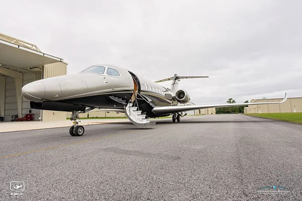 A front-quarter view of a grey and black business jet with its main door and airstairs extended on a tarmac.