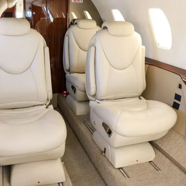 Angled view of light beige leather seats in a private jet cabin with dark wood paneling.