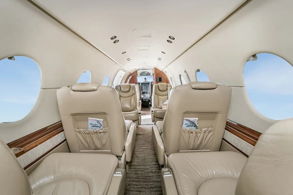 A wide view of the business jet's cabin interior, featuring rows of beige leather seats and the cockpit visible in the distance.