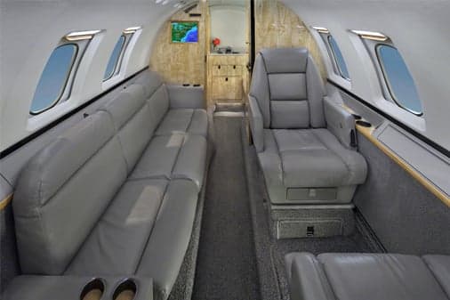 The interior cabin of a private jet featuring a grey leather sofa and a single seat.