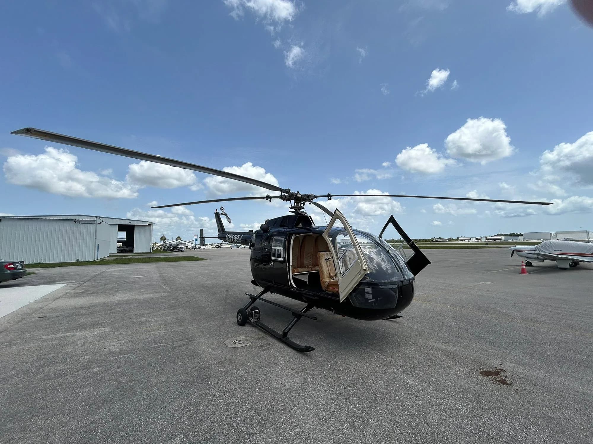 A black helicopter with an open door sits on the tarmac under a partly cloudy sky.