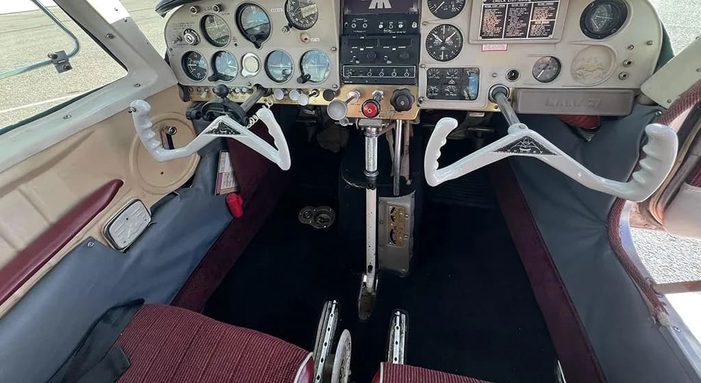 The cockpit of a small aircraft, showing the instrument panel, dual yokes, and rudder pedals.