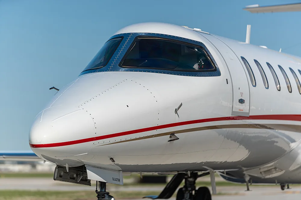 A close-up of the nose and cockpit windows of a white private jet with red and gold stripes.