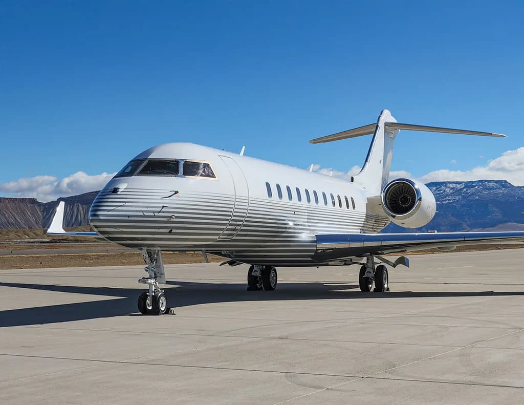 A front-side view of a white business jet with grey stripes on the fuselage, parked on an airfield.