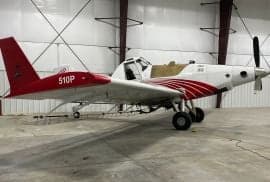 A white and red Air Tractor 510P crop duster is parked in a hangar.