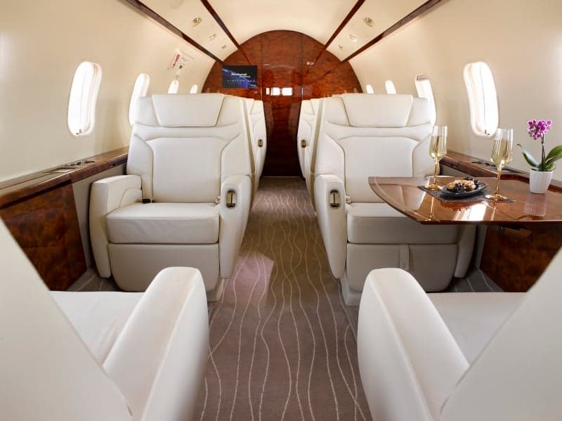 The aircraft's interior features white leather seats and wood accents.