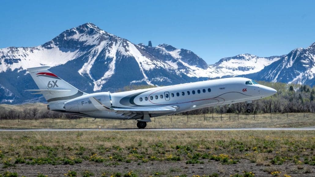 A Dassault Falcon 6X taking off with mountains in the background.