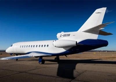A white and blue Dassault Falcon 900EX, registration C-GEOS, parked on the tarmac.