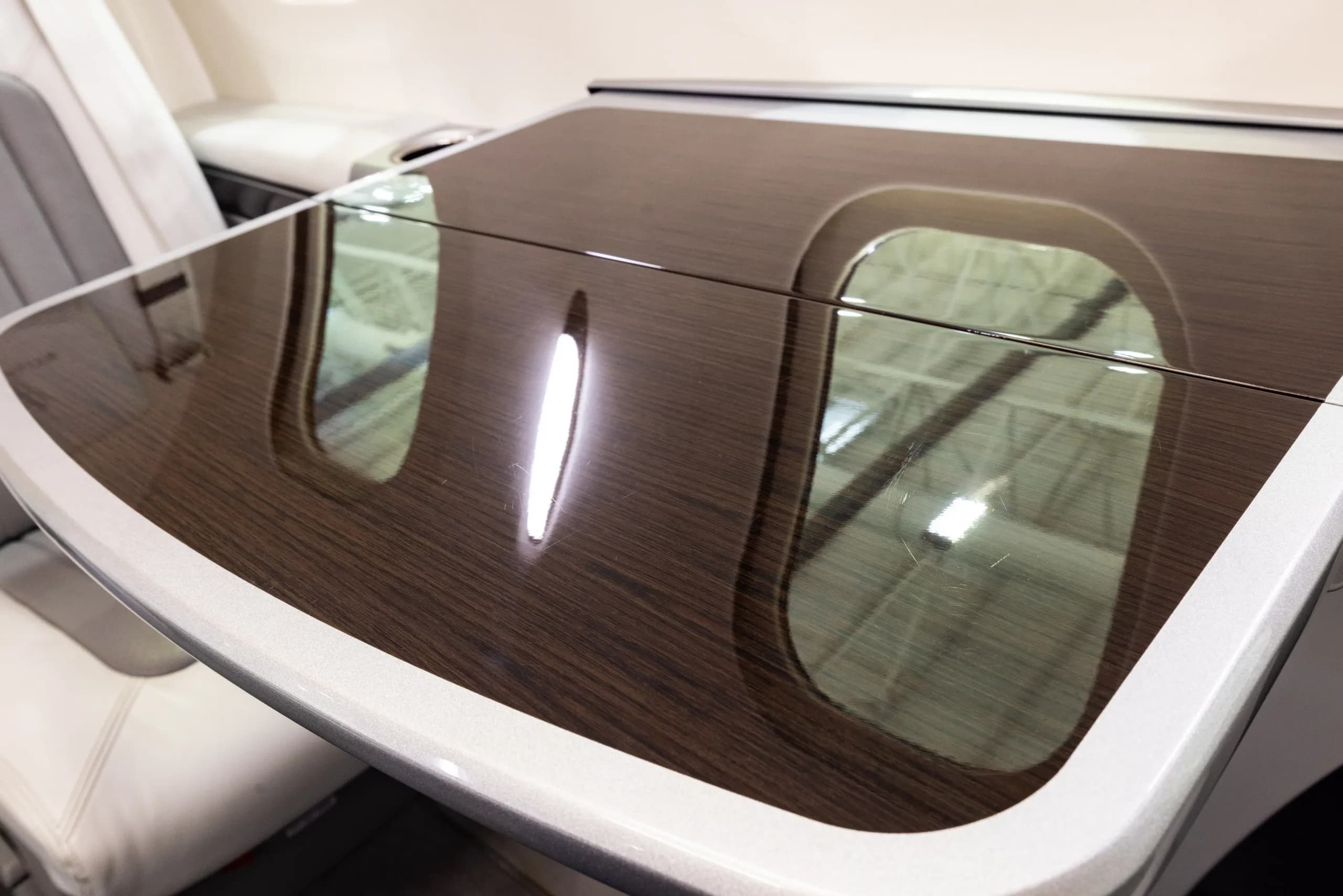 A close-up of a dark wood-grain cabin table with reflections of the aircraft windows.