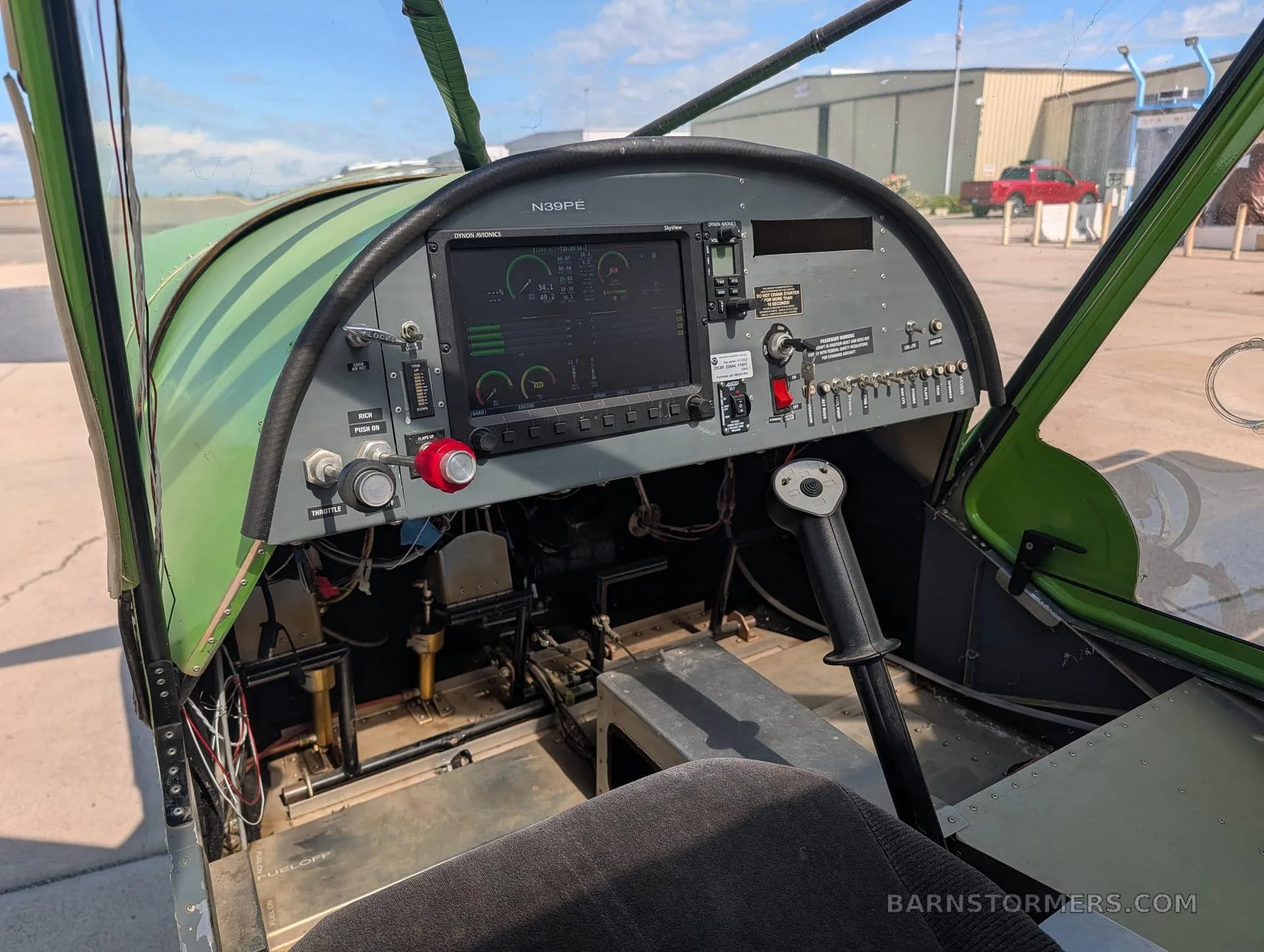 The cockpit of the green aircraft, featuring a modern digital instrument panel and a control stick.