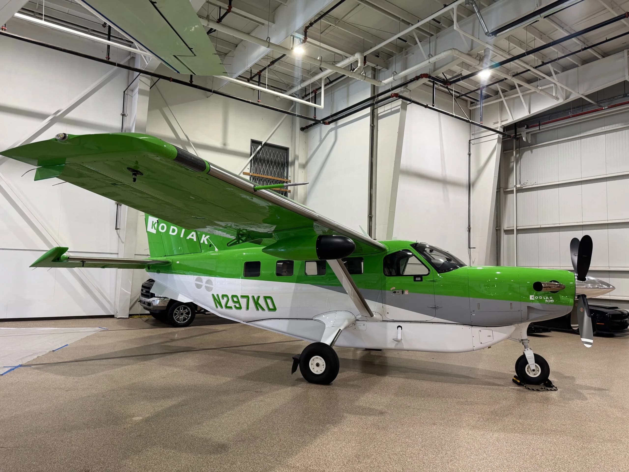 A green, white, and grey Kodiak aircraft (N297KD) parked inside a hangar.