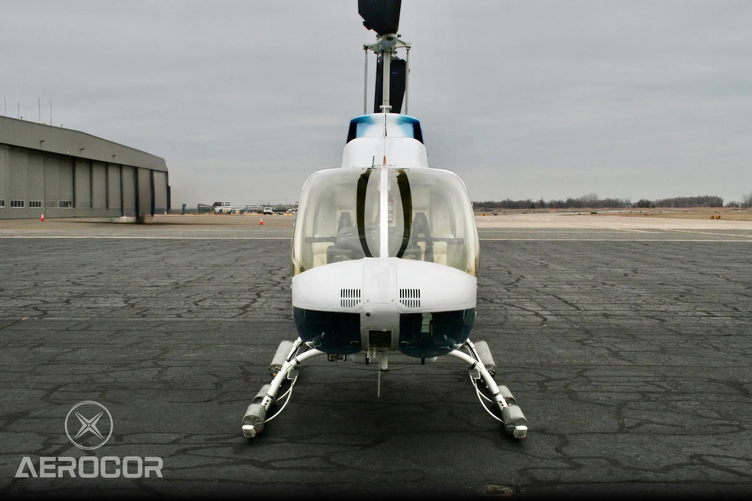 A head-on front view of the blue and white Bell JetRanger III helicopter, tail number N411DD, on an airport tarmac.