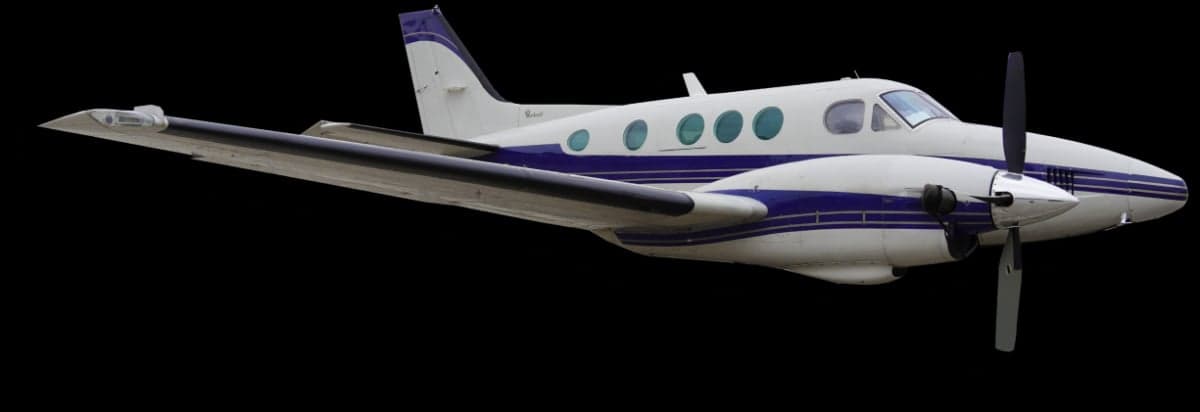 A twin turboprop aircraft in flight against a black background.