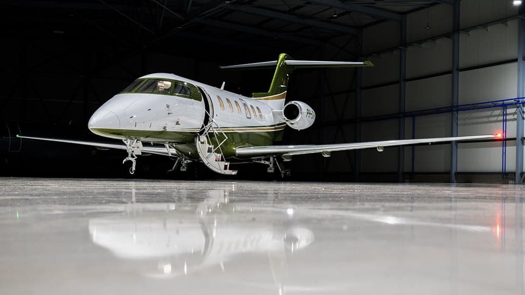 A white and green business jet with its main door open, parked in a dimly lit hangar.