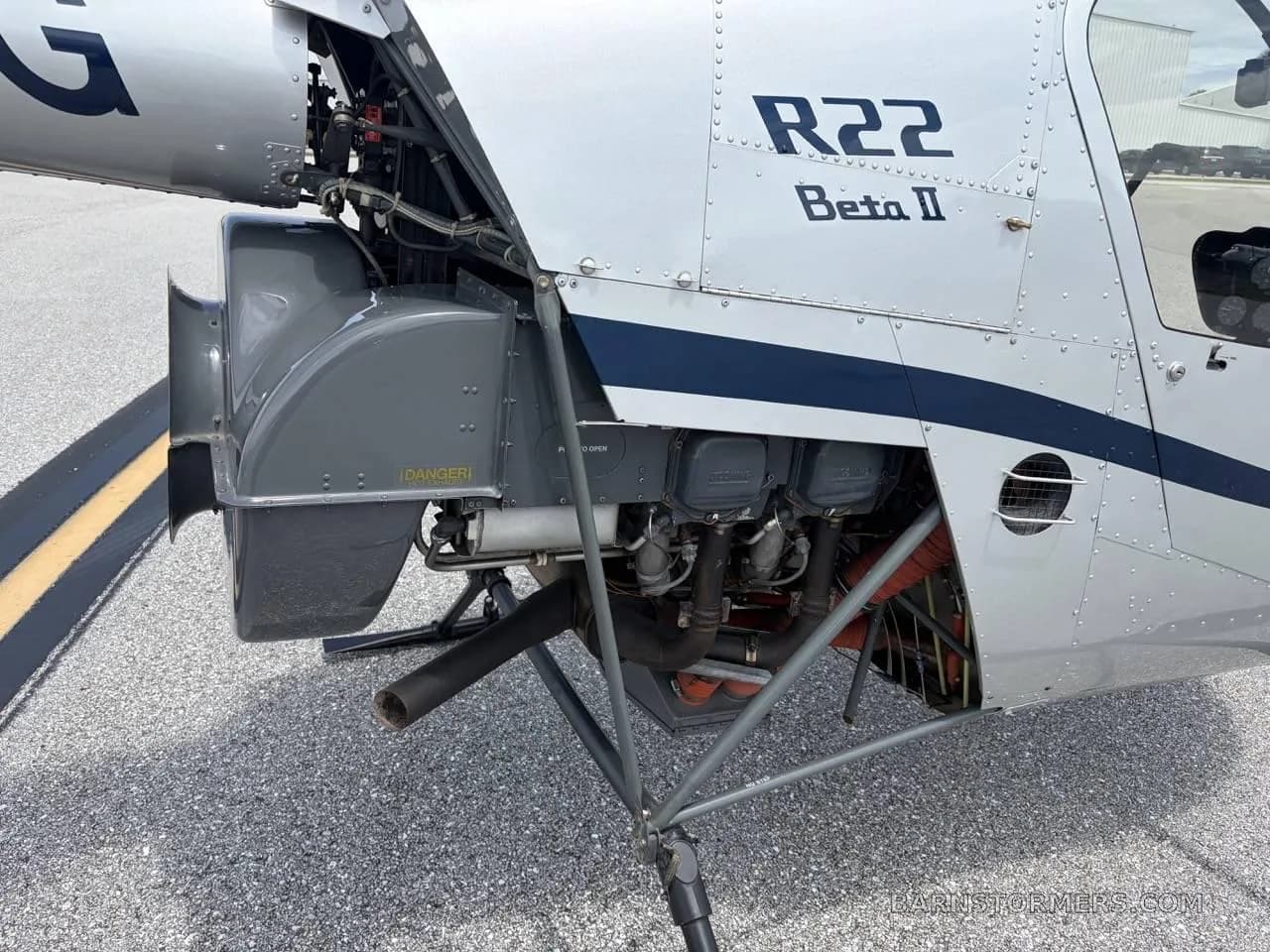 A close-up view of the exposed engine and mechanical components of a silver Robinson R22 Beta II helicopter.