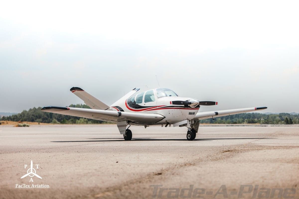 Three-quarter frontal view of a white single-engine aircraft with red and black stripes on an airfield.