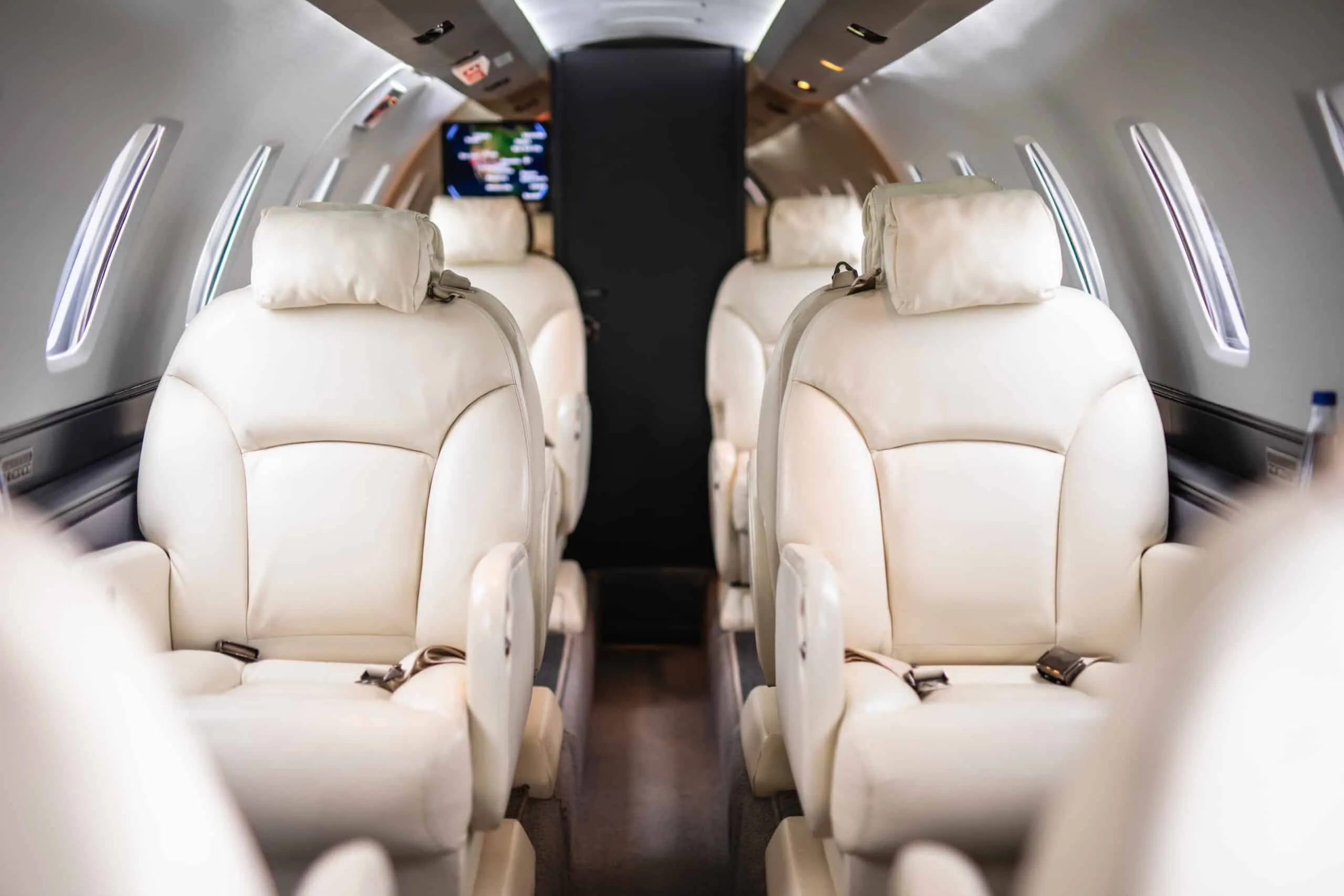 A close-up view of the light-colored leather seats in a private jet cabin, looking towards the rear.