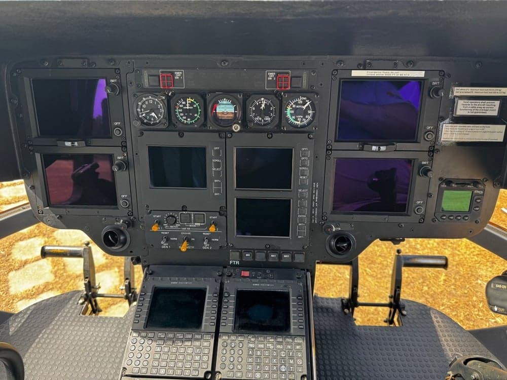 Helicopter cockpit instrument panel with multiple screens and gauges.