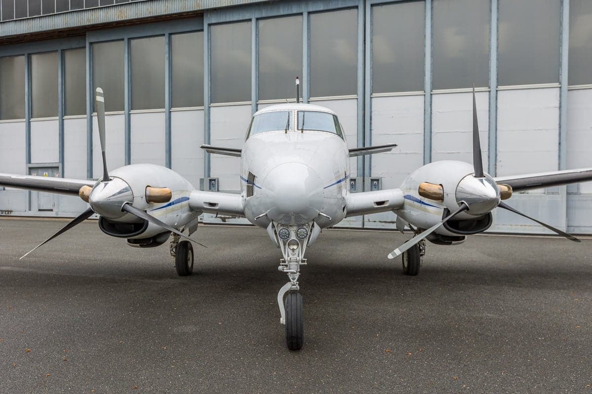 Front view of a Beechcraft King Air C90 aircraft with a white and blue paint scheme, parked on the tarmac.