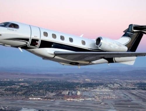 A white and black Phenom 300 jet flying over a city.