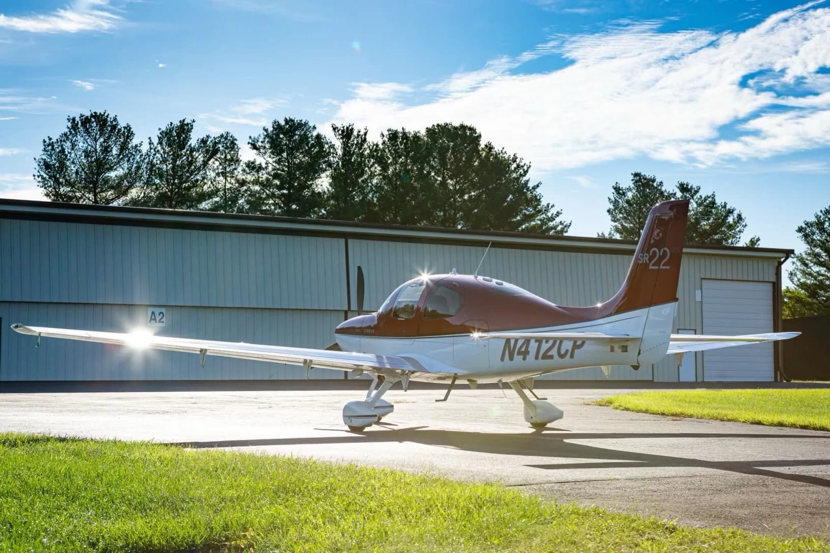 A red and white Cirrus SR22 aircraft (N412CP) parked on an airfield with sunlight reflecting off its wing.