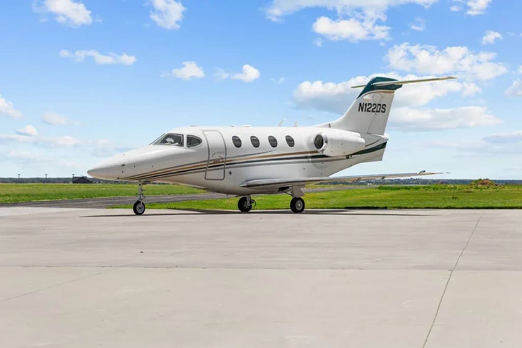 A white private jet with green and gold stripes and registration N122DS, parked on an airfield.