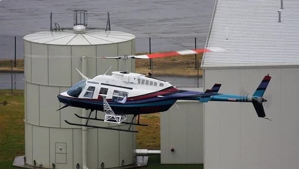 A Bell 206 Jet Ranger helicopter in flight near a building.