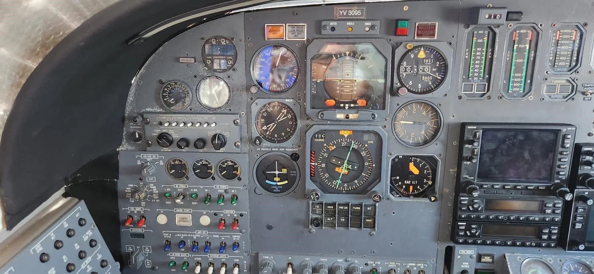 A close-up view of the left side of the cockpit instrument panel, showing analog gauges and some digital displays, with registration YV-3095 visible.