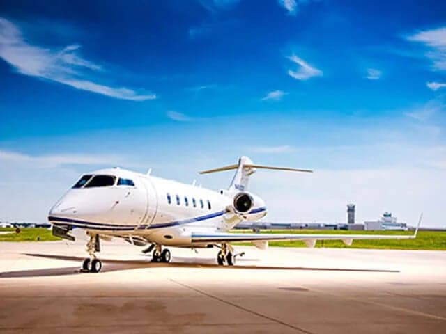 A white Bombardier Challenger business jet (N4000S) with blue accents is parked on an airfield under a blue sky.