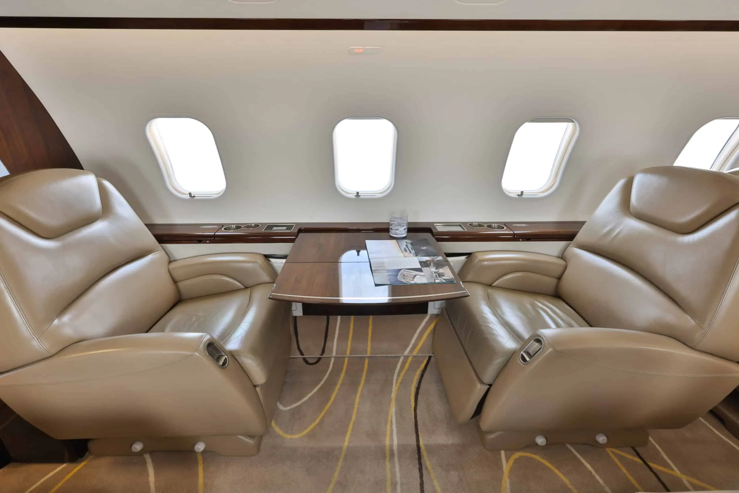 Two beige leather club seats face each other with a fold-out table in the private jet cabin.