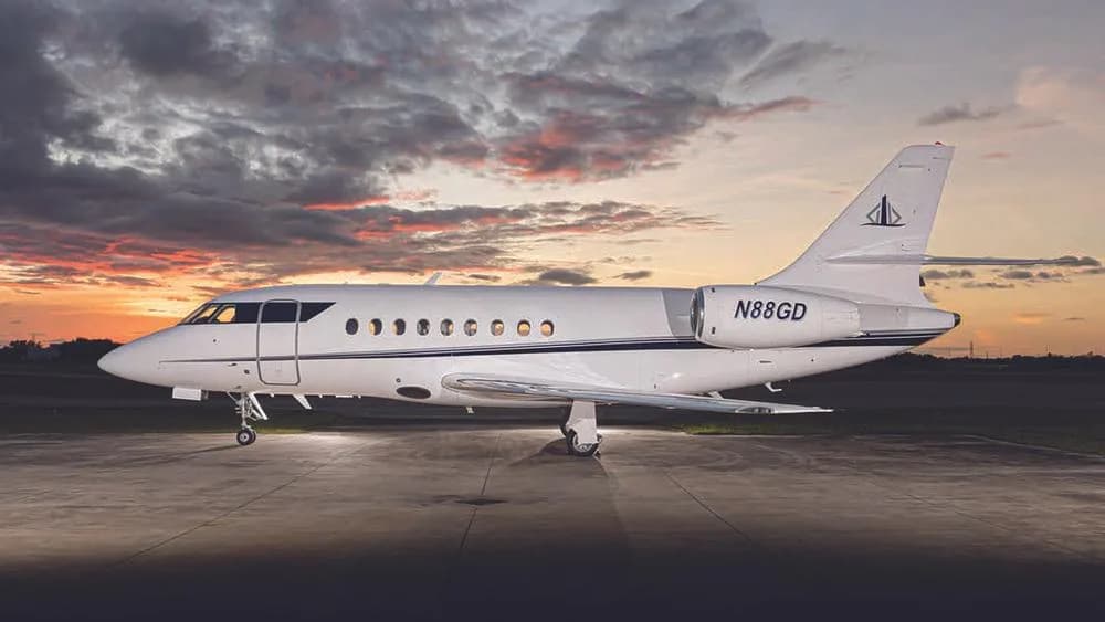A white business jet, N88GD, with a dark blue stripe, parked on an tarmac at sunset.