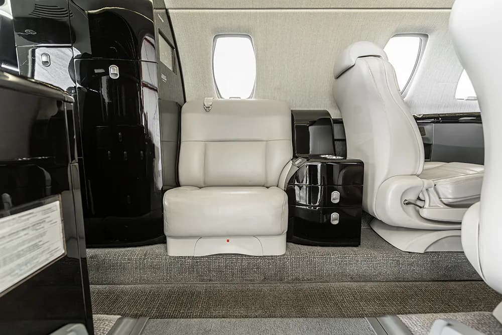 A close-up of a single light grey seat in the private jet cabin, adjacent to a black storage cabinet.