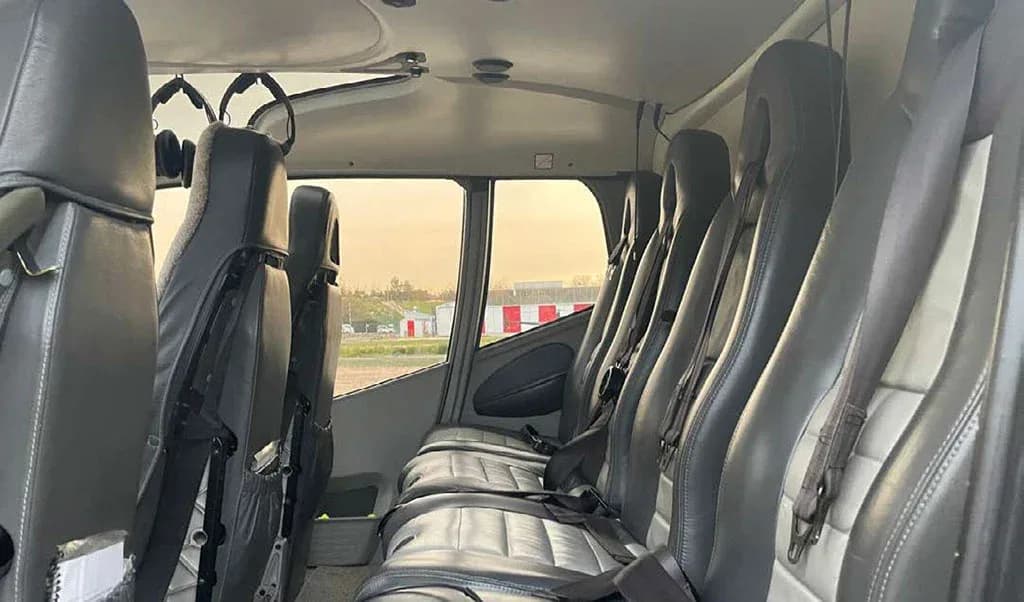 The interior of the helicopter shows rows of grey and black passenger seats with seatbelts.