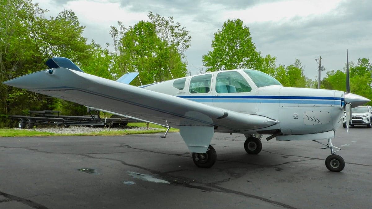 A white and blue Beechcraft Bonanza parked on the tarmac.