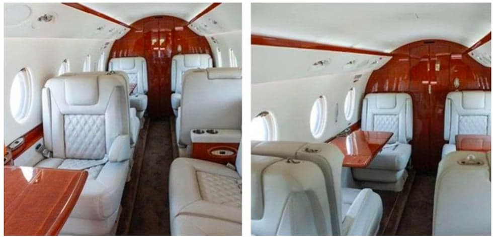 Interior view of the aircraft cabin with white leather seats and wooden tables.