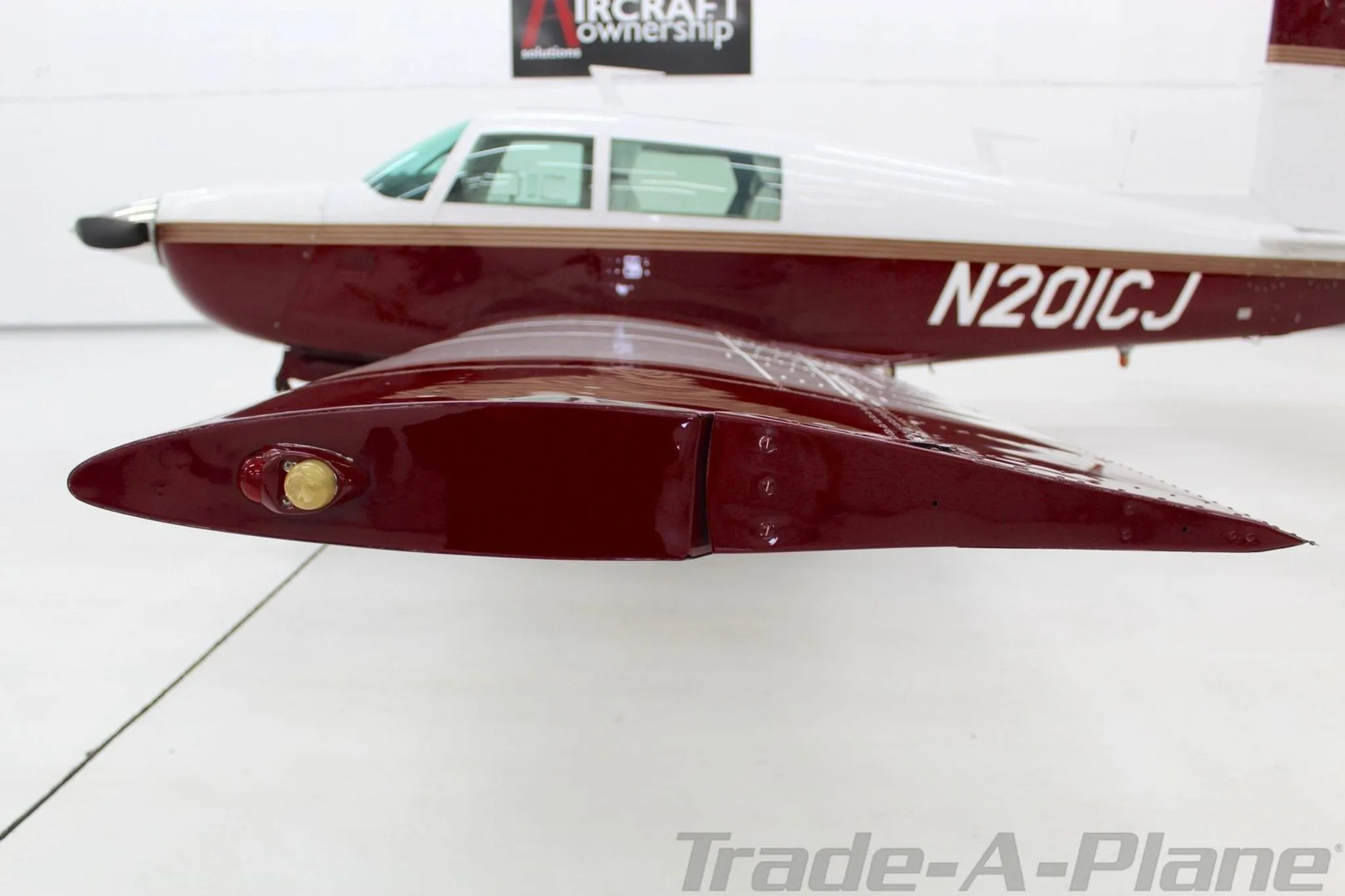 A side view of the Mooney M20J's wingtip and part of the fuselage, showing the maroon paint and navigation light.