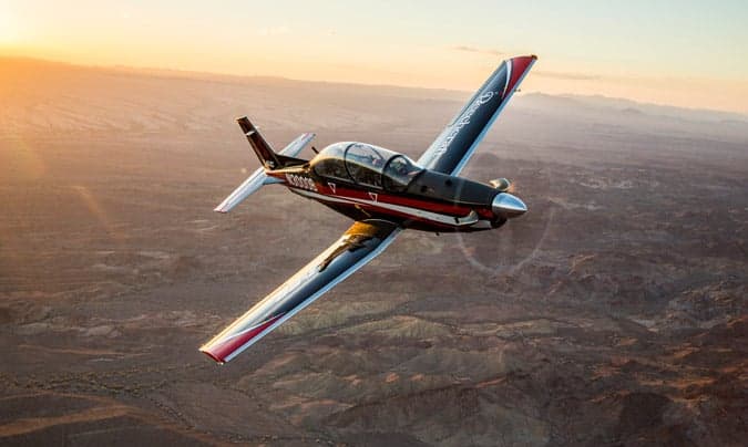 A Beechcraft T-6C Texan II aircraft in flight against a sunset backdrop.