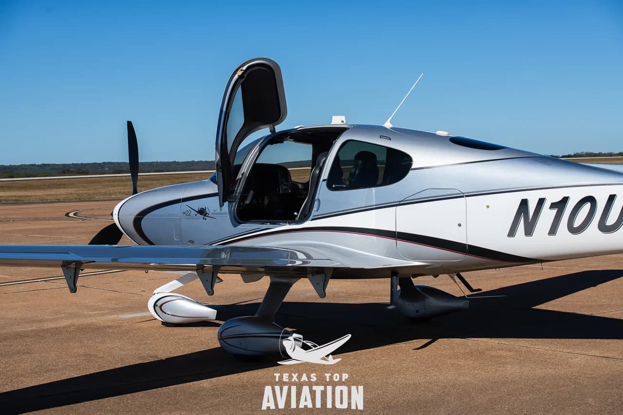 Side view of a silver and white Cirrus SR22 aircraft (N10UA) with its passenger door open.