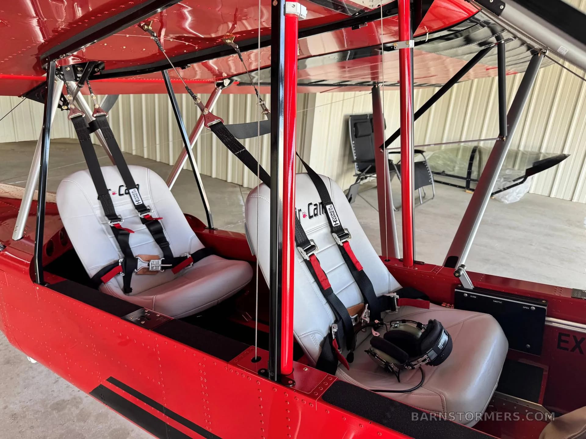 The two white seats with black harnesses inside the red Air-Cam aircraft cabin.