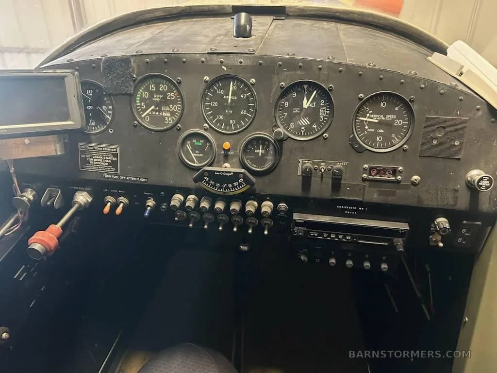 The cockpit instrument panel of a small aircraft, featuring analog gauges, switches, and a radio.