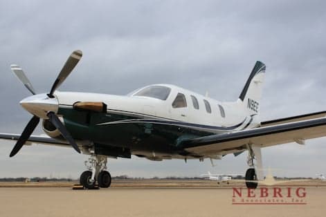 A white and dark green single-engine turboprop aircraft, N9EE, is parked on a tarmac under a cloudy sky, viewed from the front three-quarter.