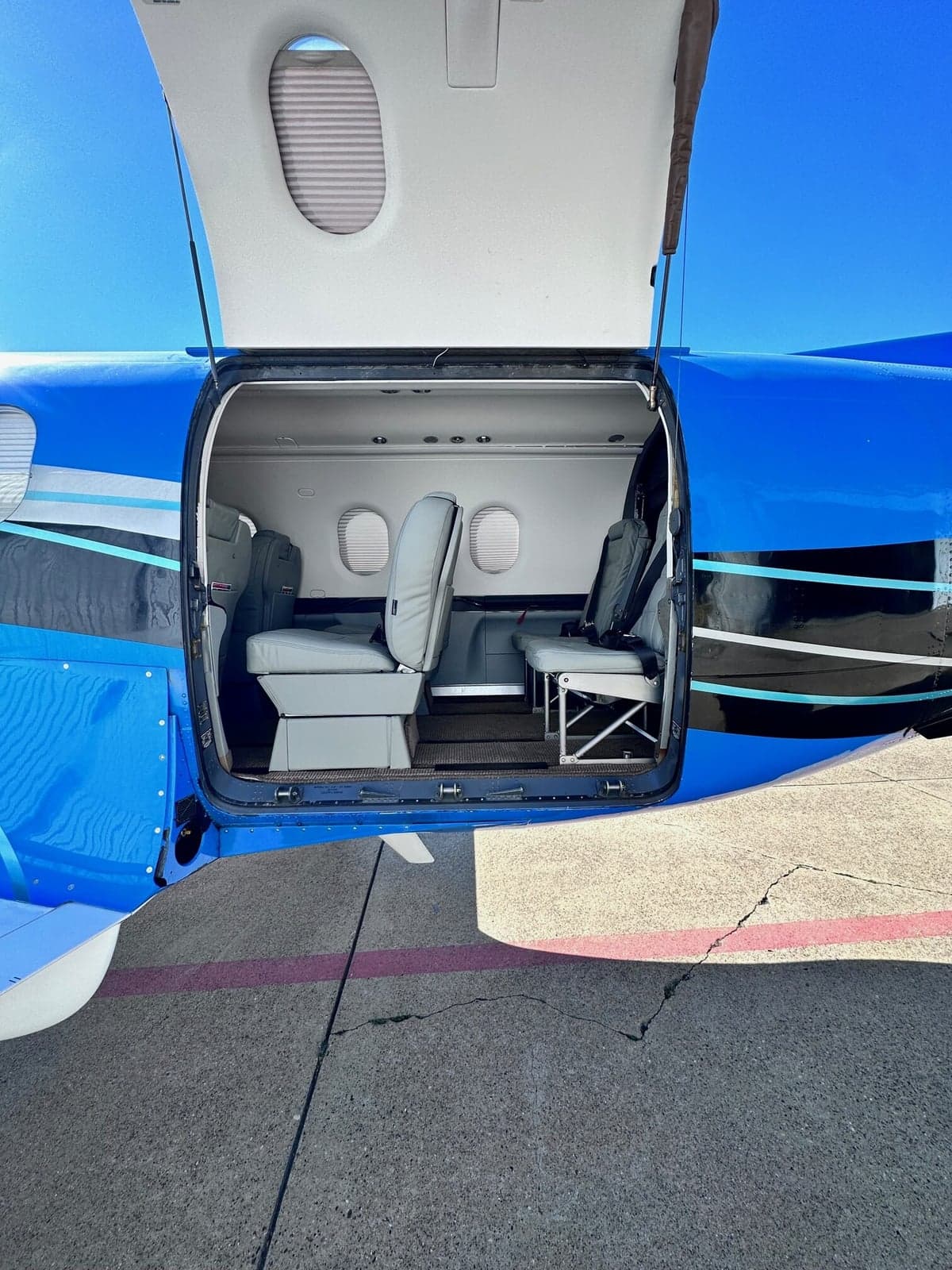 The interior of the aircraft features gray leather seats and a brown carpet, as seen from the open door.