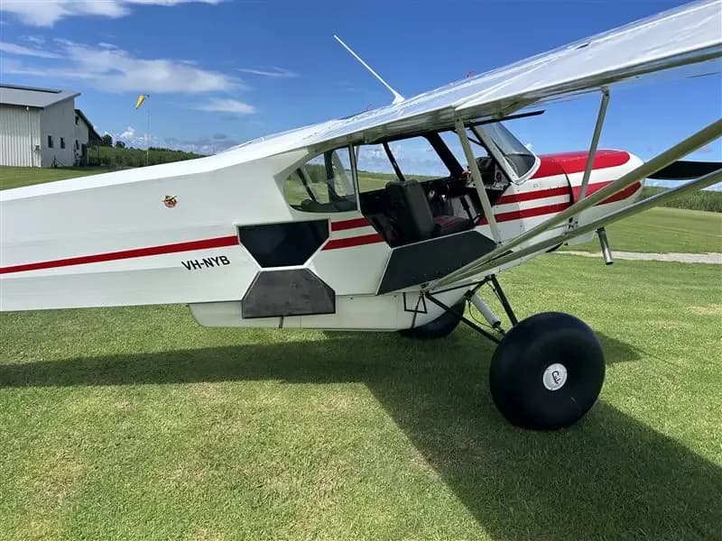 A side view of the white and red Super Cub with its door open, revealing the interior, parked on a grassy field.
