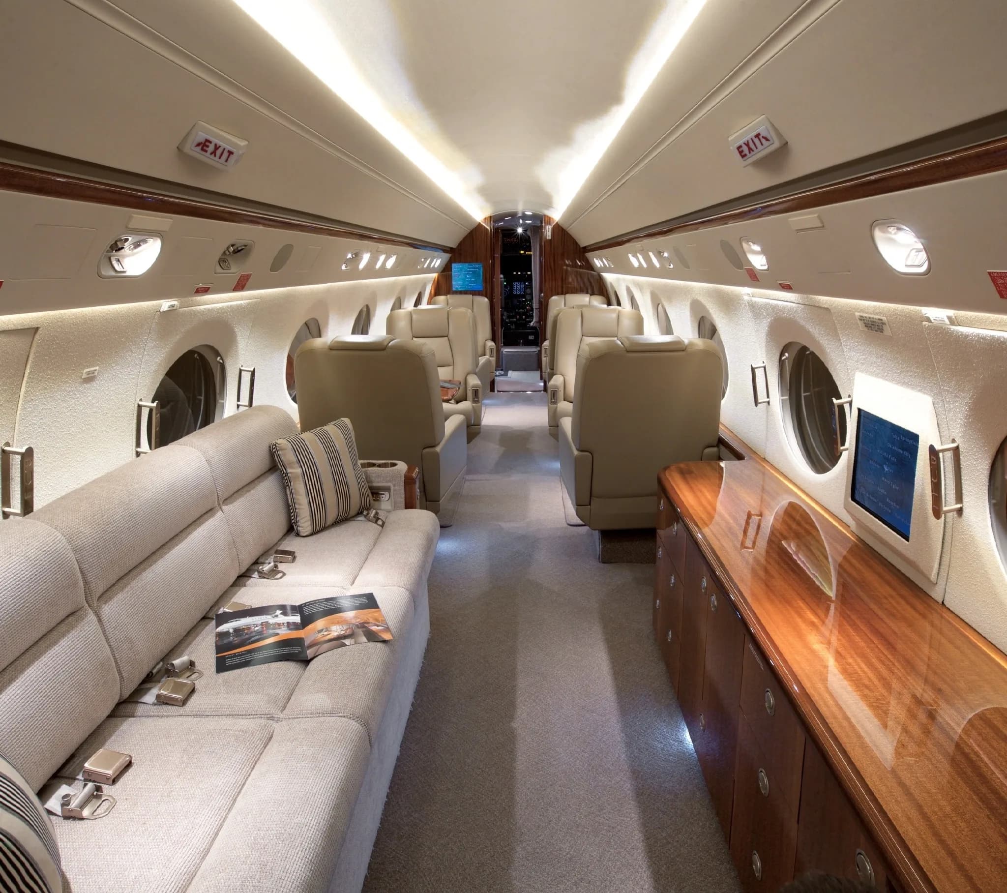 The luxurious interior cabin of a private jet features a light-colored sofa and individual seats with wood accents.