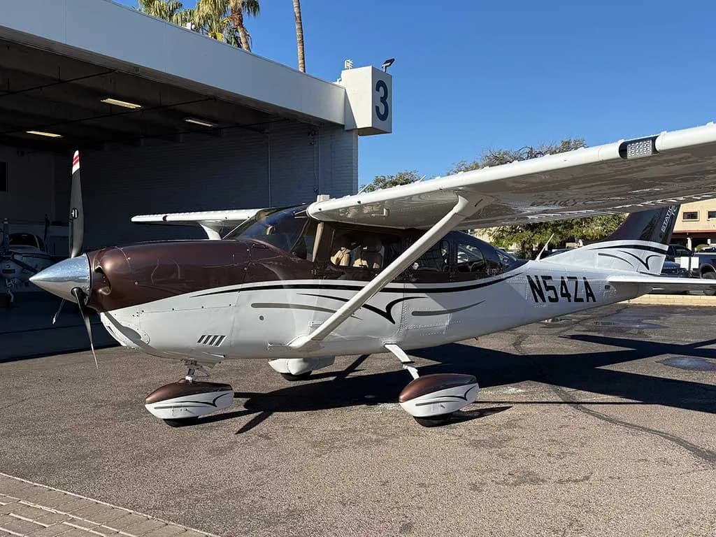 A front three-quarter view of the brown and white Cessna 182 Skylane N54ZA parked on an airfield.