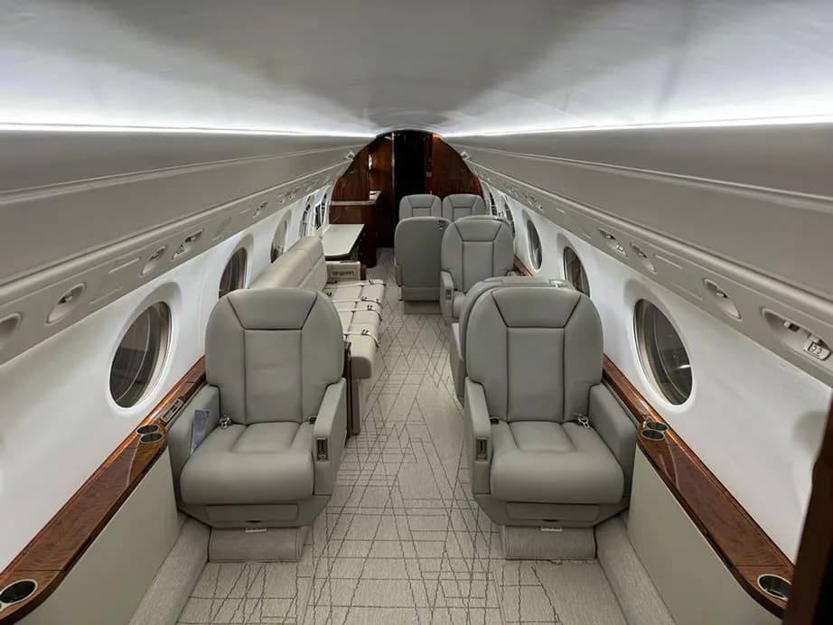 A view of the aircraft cabin from the front, showing light gray leather seats, a sofa, and wooden accents.