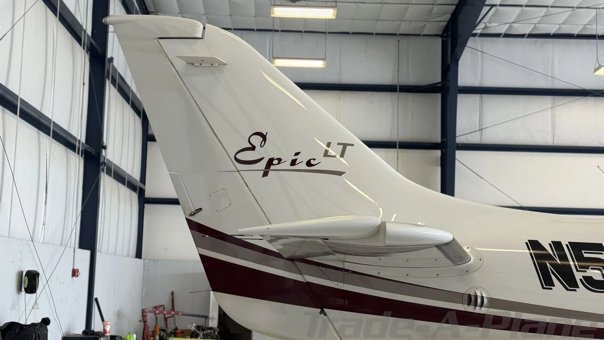 Close-up of the tail of a white Epic LT aircraft with a dark red stripe and N5819X registration, showing the "Epic LT" logo.