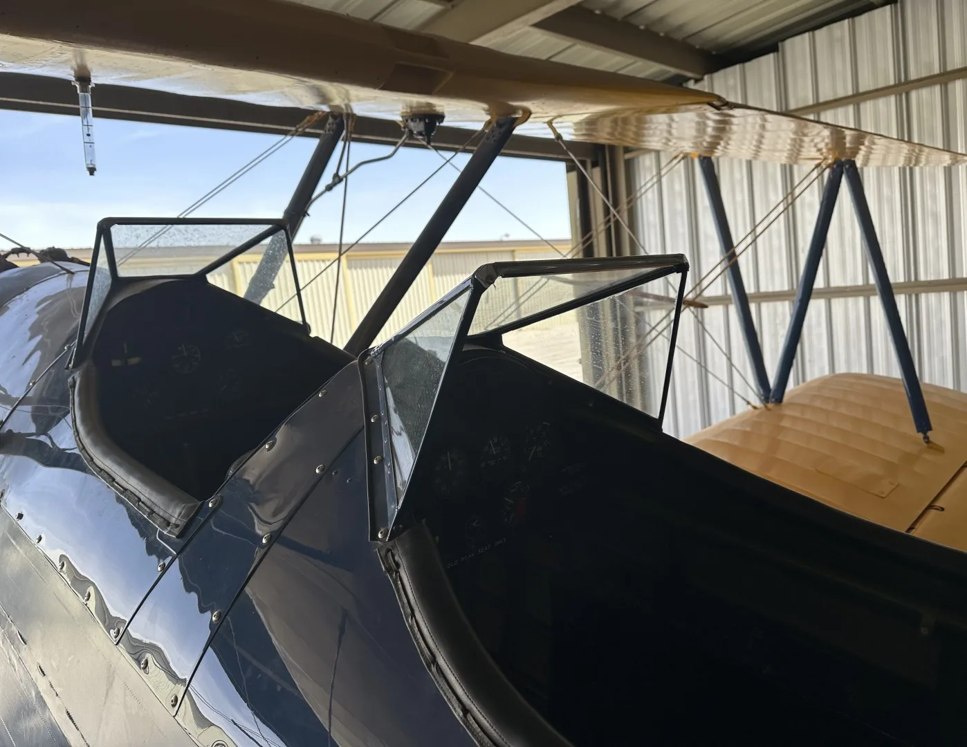 A view into the two open cockpits of a blue biplane, showing the windshields and internal structure.
