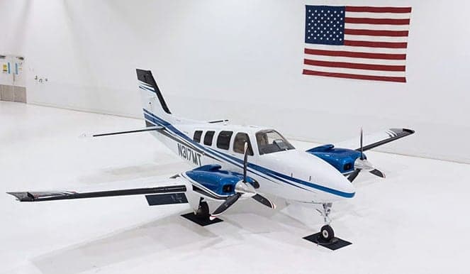 A white and blue twin-engine turboprop is parked in a hangar with an American flag.